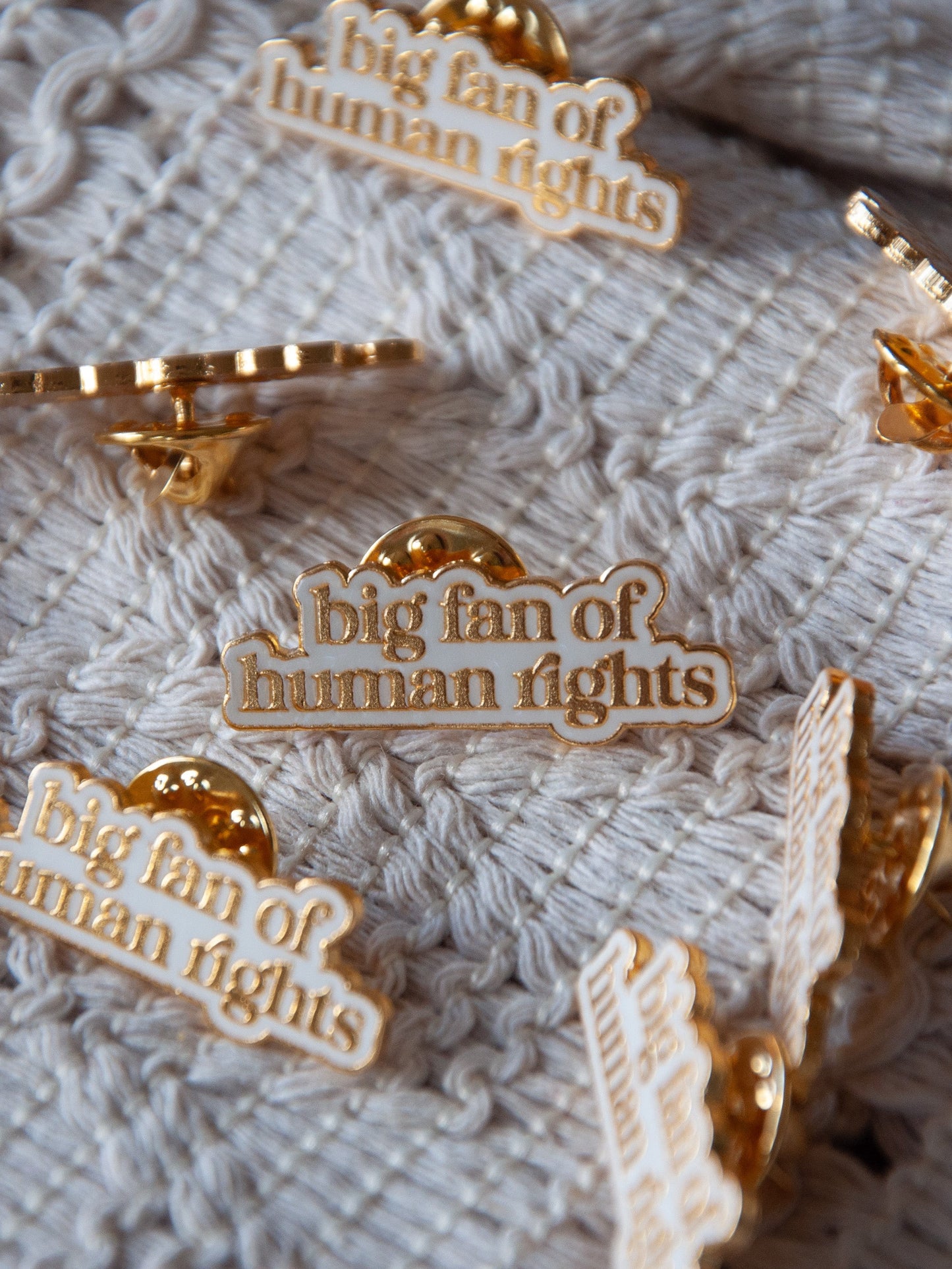 Gold pins with 'big fan of human rights' text on a textured fabric background